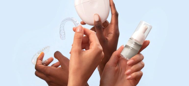 Hands holding clear braces and teeth whitening serum.